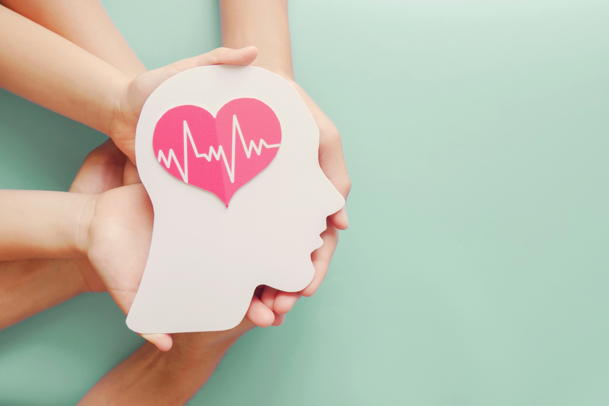 Hands holding a cutout of head with a heart where the brain should be